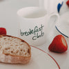Frühstücksszene mit Brot und Erdbeeren, davor die kleine Tasse mit grünem „breakfast club“-Schriftzug.