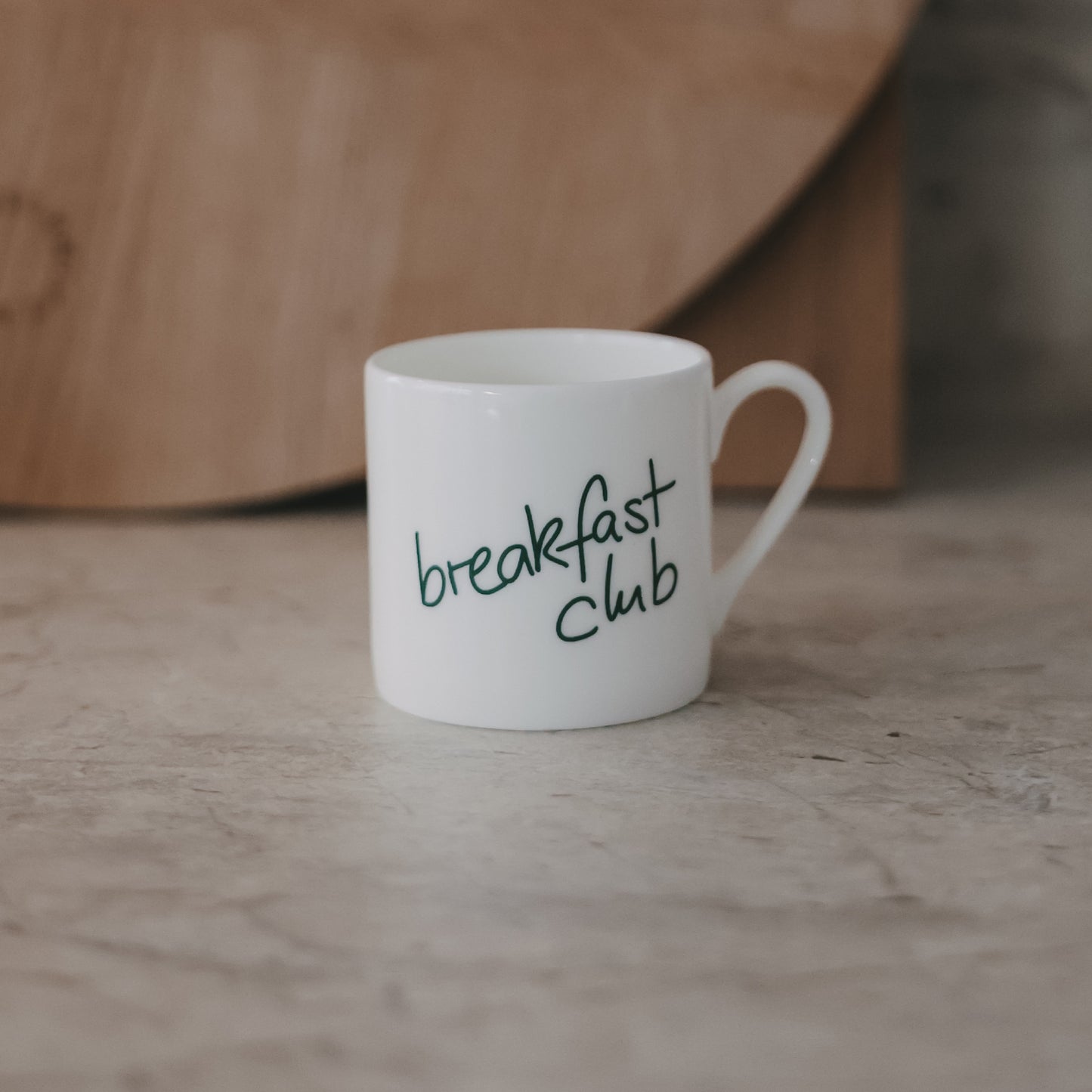 Kleine Tasse mit grünem „breakfast club“-Schriftzug, minimalistisch auf Steinfläche fotografiert.