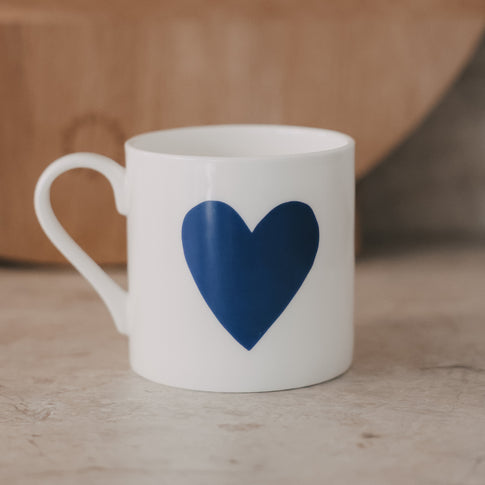 Weiße Tasse mit großem dunkelblauen Herz auf der Vorderseite vor neutralem Hintergrund