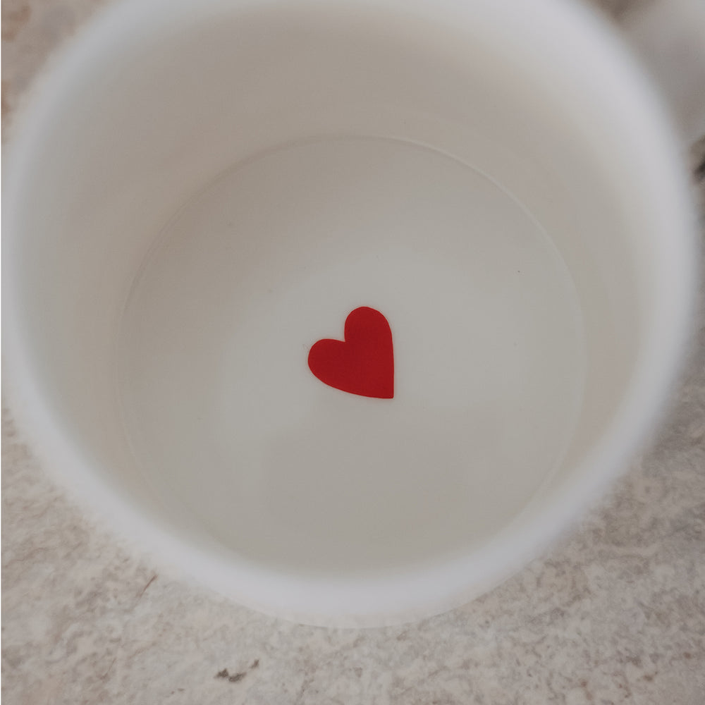 Weiße Tasse mit kleinem rotem Herz im Inneren auf hellem Untergrund