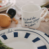 Weiße Tasse mit blauem Schriftzug „Es sind die kleinen Dinge im Leben“, dekoriert auf gedecktem Tisch mit Teller und Obst & Gemüse im Hintergrund