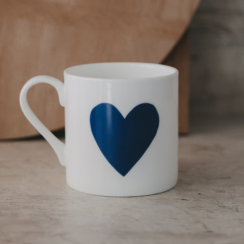 Weiße Tasse mit blauem großem Herz vor warmem Holz-Hintergrund