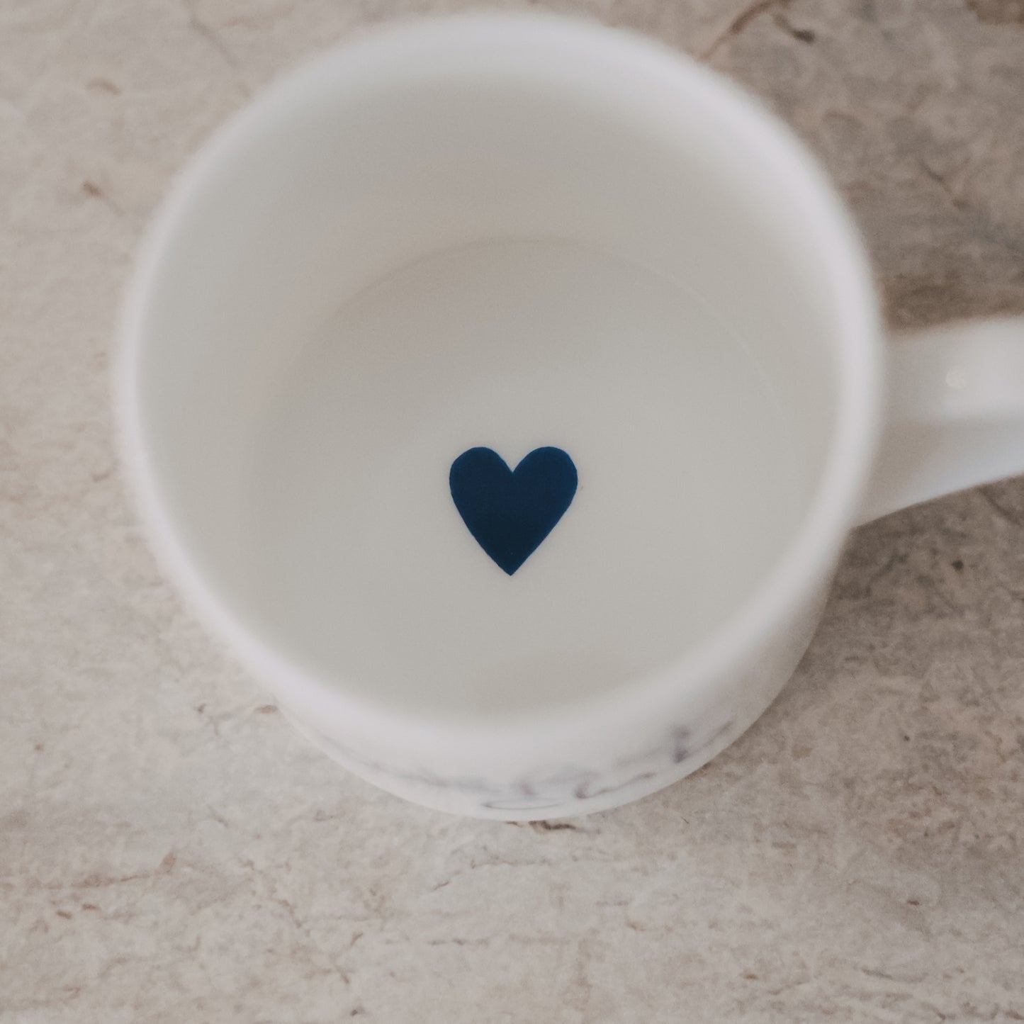 Weiße Tasse mit dunkelblauem Herz auf der Innenseite, Draufsicht auf hellem Untergrund