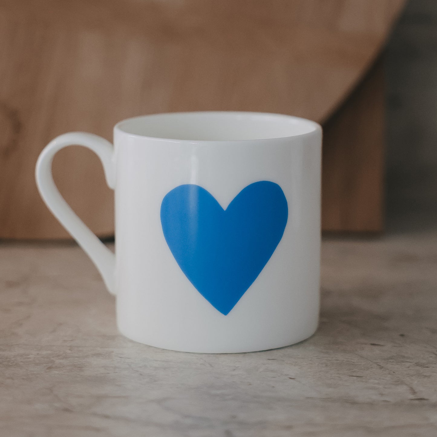 Weiße Tasse mit großem blauem Herzmotiv auf der Außenseite vor schlichtem Hintergrund