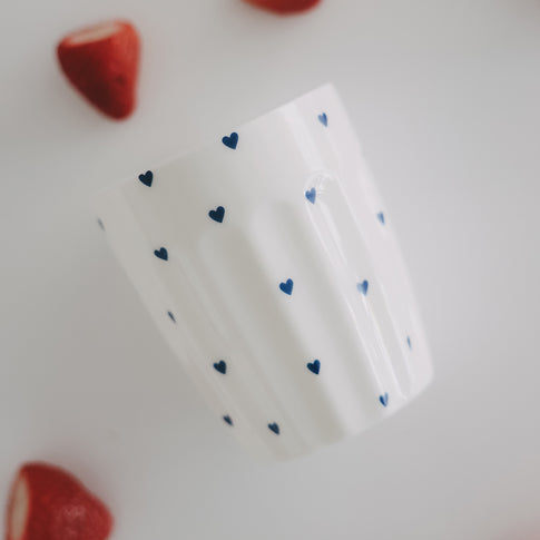 Weißer Becher mit blauen Herzen, schräg fotografiert, modernes minimalistisches Design