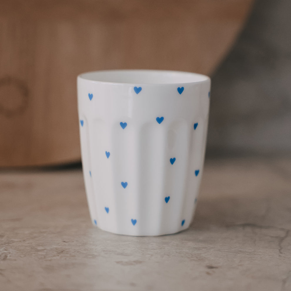 Weißer Porzellanbecher mit kleinen blauen Herzen auf Tisch, minimalistisches Design