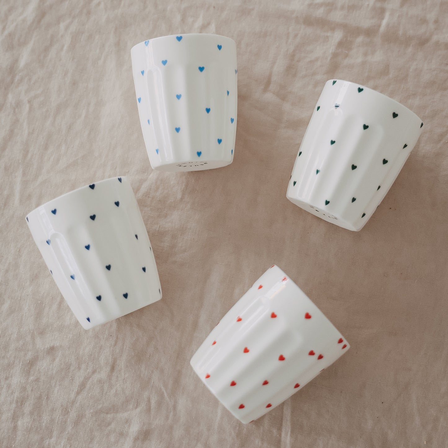 Mehrere Porzellanbecher mit Herzmuster in Blau, Grün und Rot auf Stoff drapiert