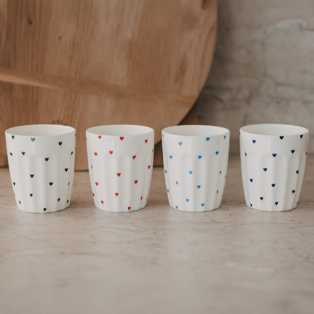 Vier Becher mit kleinen Herzmotiven in verschiedenen Farben nebeneinander