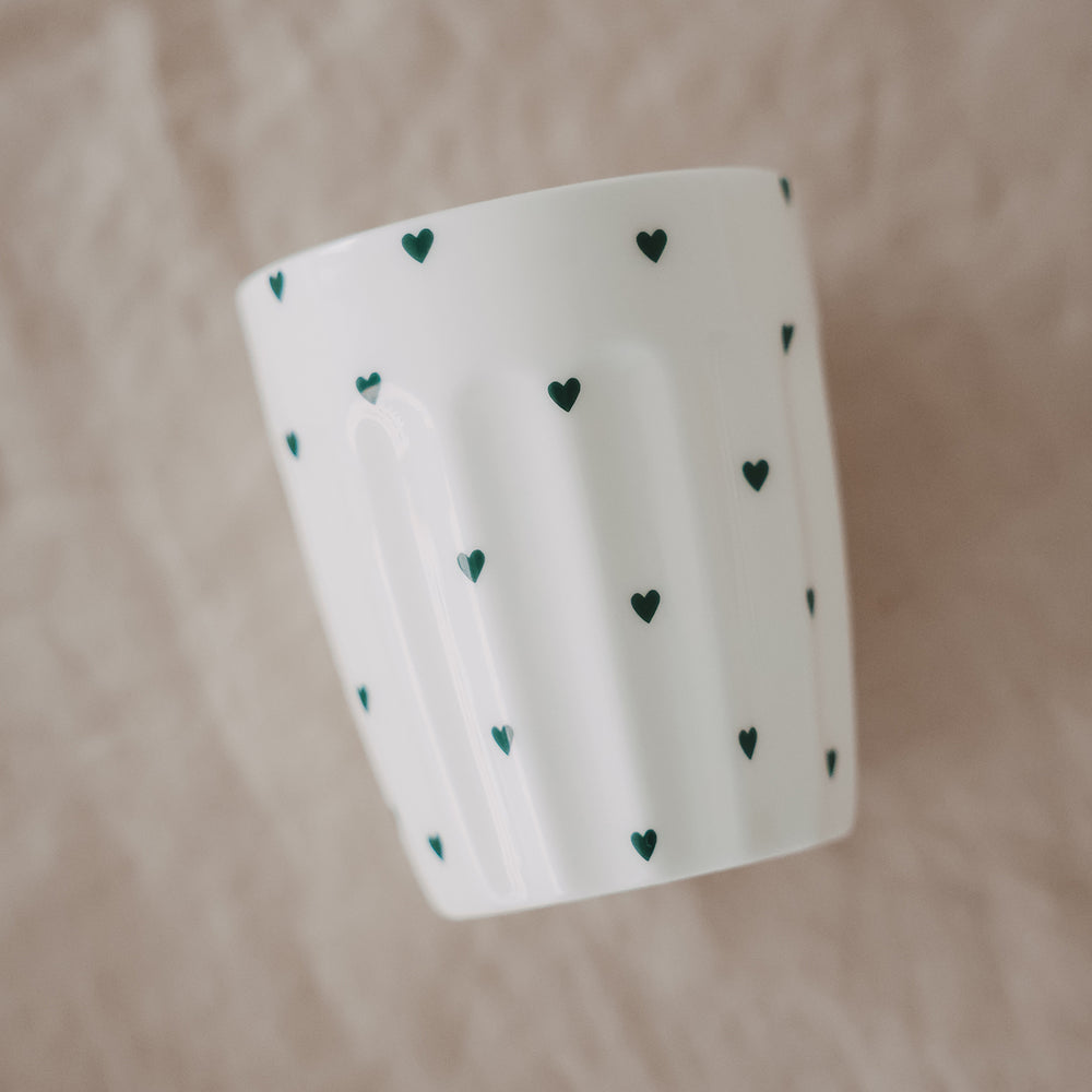 Weißer Becher mit grünen Herzchen im schrägen Winkel, schlichtes Design, handgefertigt