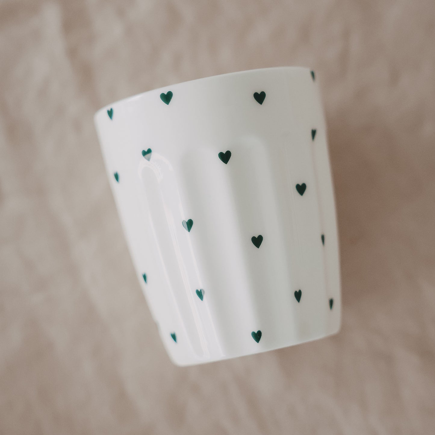 Weißer Becher mit grünen Herzchen im schrägen Winkel, schlichtes Design, handgefertigt