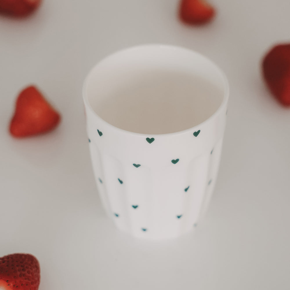 Keramikbecher mit grünen Herzen, umgeben von frischen Erdbeeren auf hellem Hintergrund