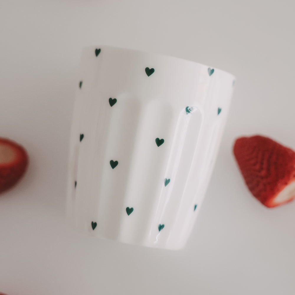 Weißer Becher mit grünen Herzchen und Erdbeeren, modernes Food- und Lifestyle-Setting