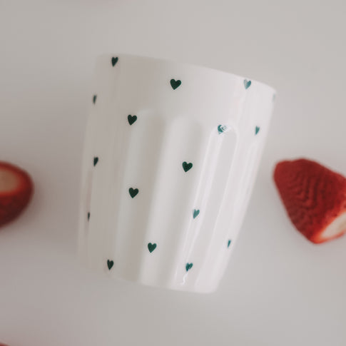Weißer Becher mit grünen Herzchen und Erdbeeren, modernes Food- und Lifestyle-Setting