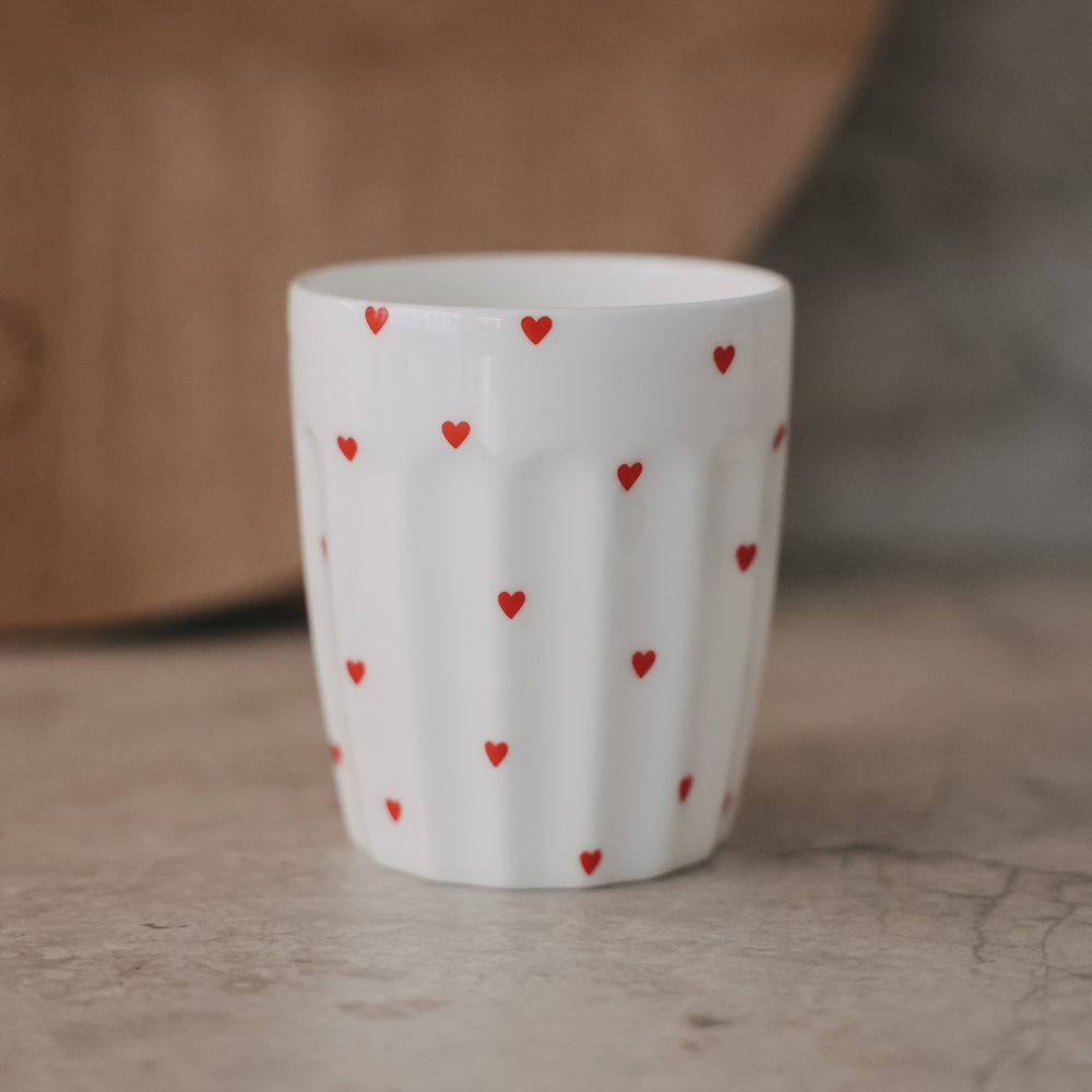 Weißer Becher mit kleinen roten Herzen auf Tisch, minimalistisch, Keramik Tasse für Kaffee oder Tee