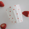 Weißer Becher mit roten Herzen zwischen Erdbeeren, stilvolle Food-Fotografie