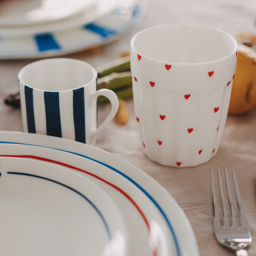 Herz-Becher neben gestreiftem Geschirr und Besteck, modernes Tischgedeck mit Keramikgeschirr