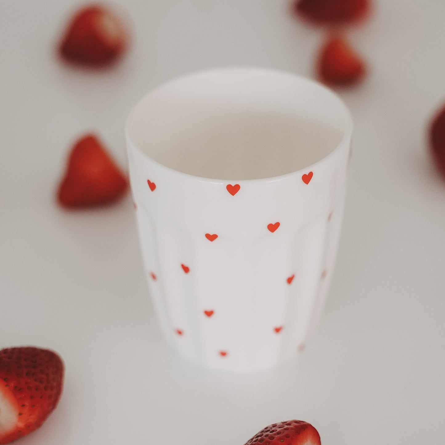 Weißer Herz-Becher umgeben von frischen Erdbeeren, sommerliche Szene, Keramik Tasse