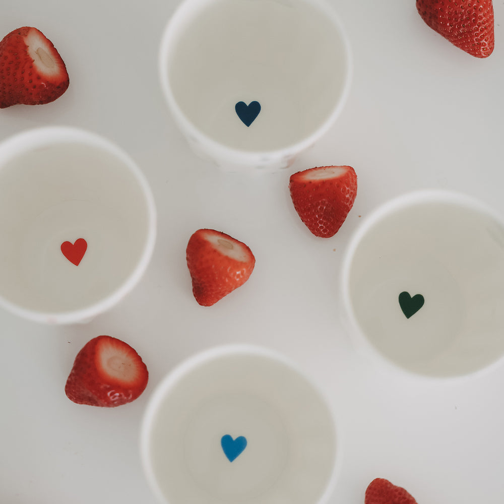 Mehrere Becher mit farbigen Herzmotiven und Erdbeeren, dekorative Anordnung von Keramiktassen