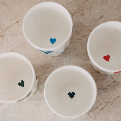 Vier Keramikbecher mit bunten Herzmotiven von oben, dekorativ angeordnet
