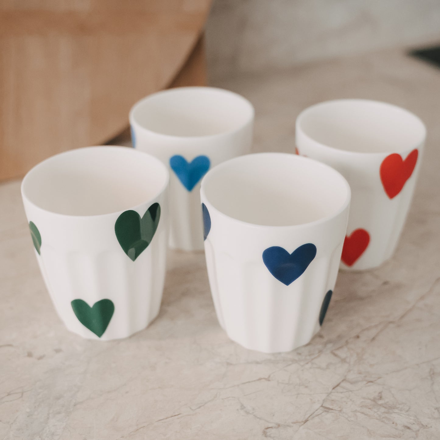 Weiße Becher mit großen Herzmotiven in Blau, Grün und Rot, modern arrangiert