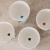 Innenansicht von Keramikbechern mit kleinen Herzmotiven am Boden in verschiedenen Farben