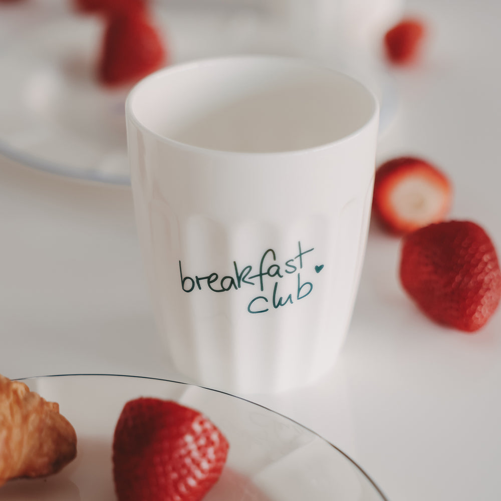 Keramikbecher „breakfast club“ mit grünem Schriftzug neben Erdbeeren, Frühstücks-Setting