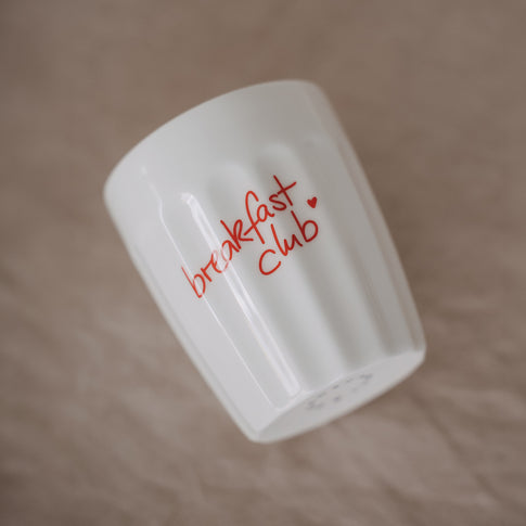 Weißer Keramikbecher „breakfast club“ mit rotem Schriftzug im Frühstücks-Setting mit Erdbeeren