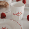 Keramikbecher „breakfast club“ mit rotem Schriftzug neben Teller und Erdbeeren, Frühstücksszene