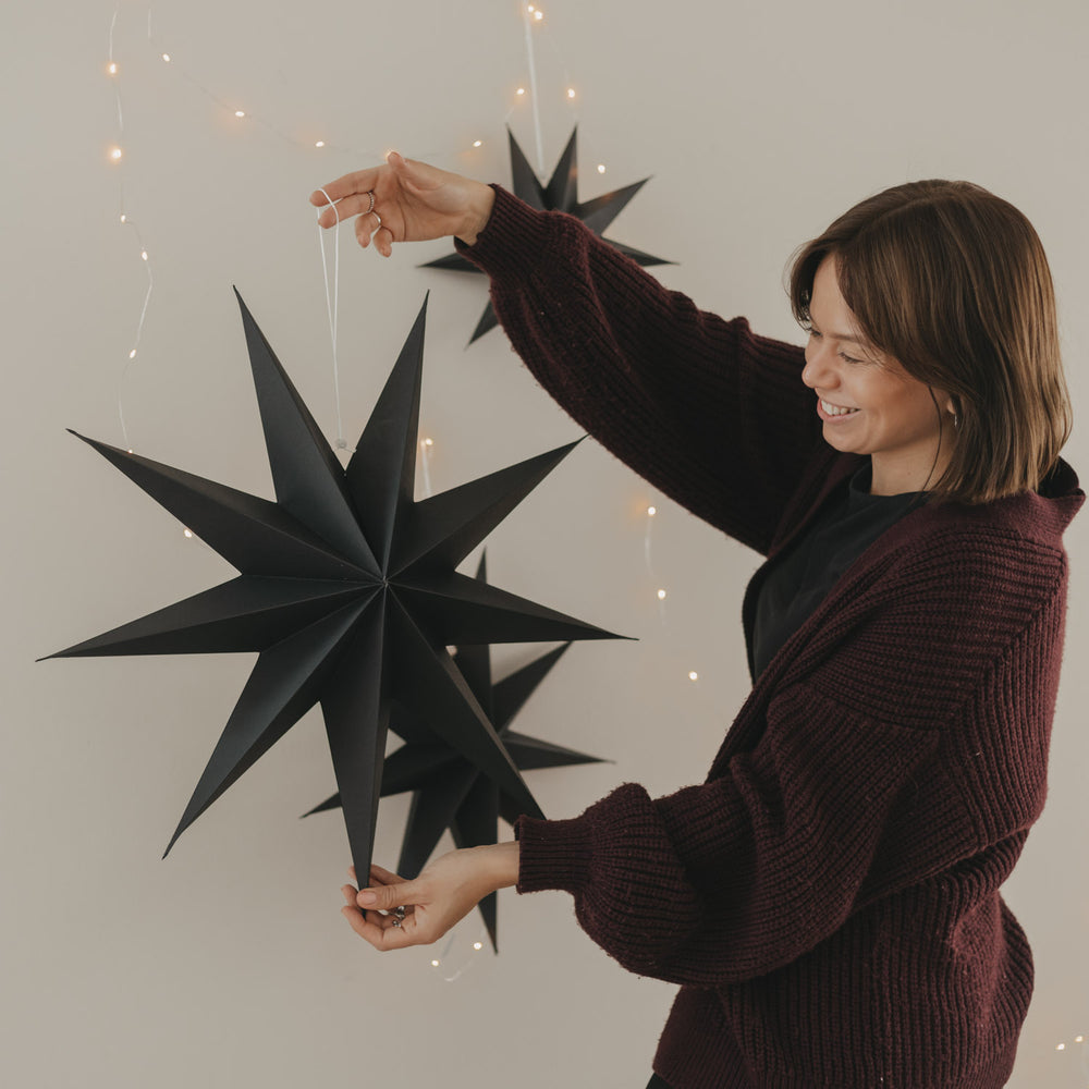 Großer schwarzer Papierstern mit Aufhängung und Lichterkette als moderne Weihnachtsdekoration