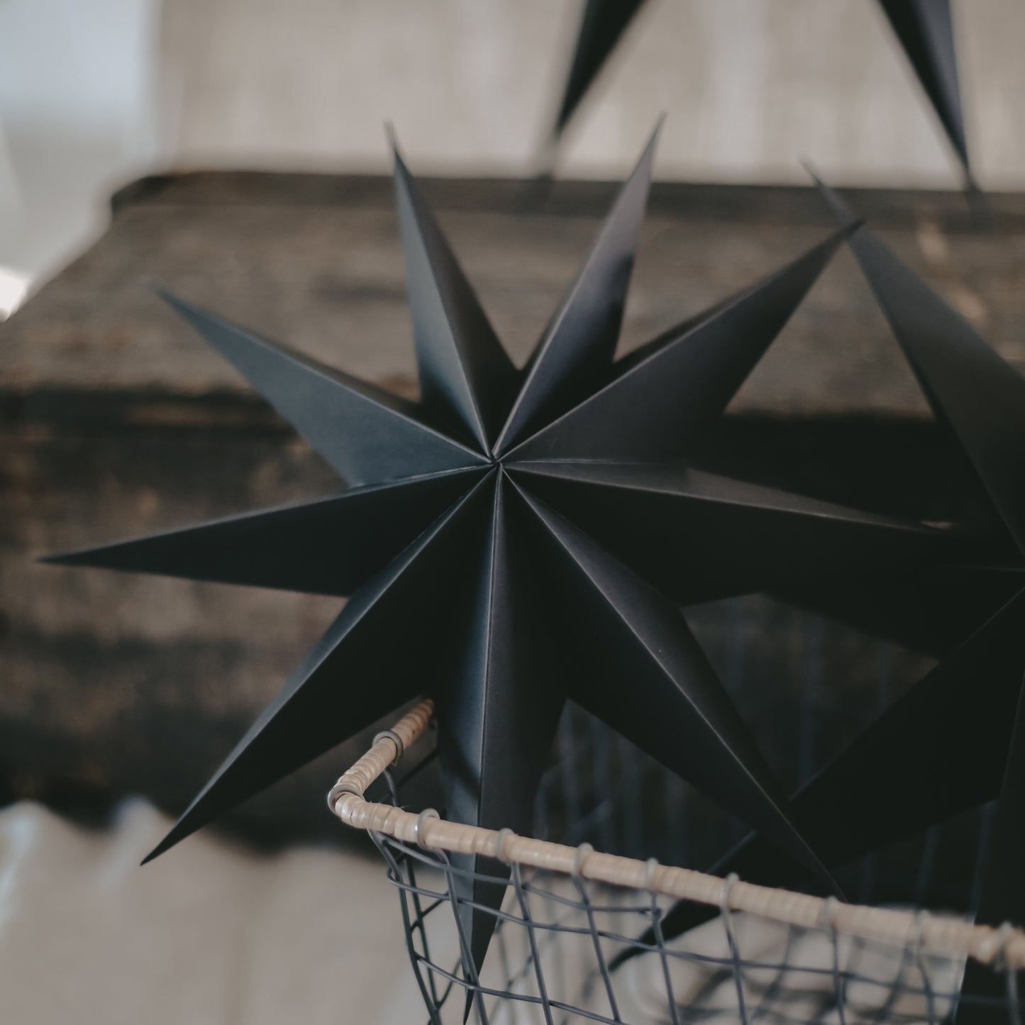 Nahaufnahme eines schwarzen Papiersterns mit 3D-Faltung in einem Drahtkorb auf rustikalem Untergrund.