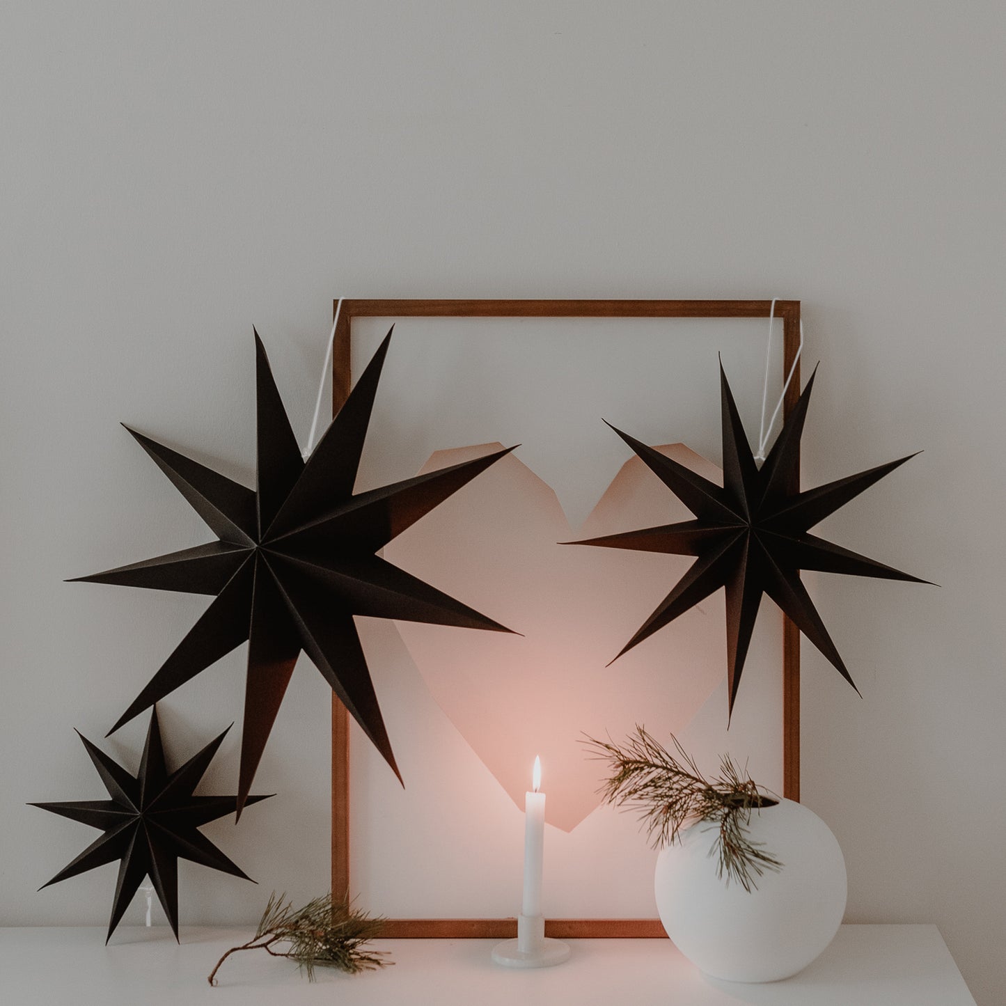 Drei schwarze Papiersterne als Wanddeko mit Kerze und Bilderrahmen – stilvolle Weihnachtsstimmung im Interior.