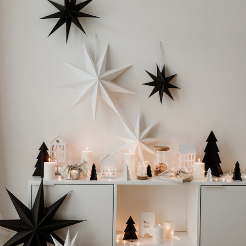 Weihnachtliche Deko mit schwarzen und weißen Papiersternen an der Wand über einem stimmungsvoll dekorierten Sideboard.