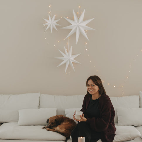 Weiße Papiersterne mit Lichterkette als minimalistische Weihnachtsdeko über einem weißen Sofa