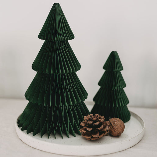 Minimalistisches Weihnachtsarrangement mit zwei dunkelgrünen Papiertannen in verschiedenen Größen auf einem weißen Teller, dekoriert mit einem Tannenzapfen und einer Walnuss.