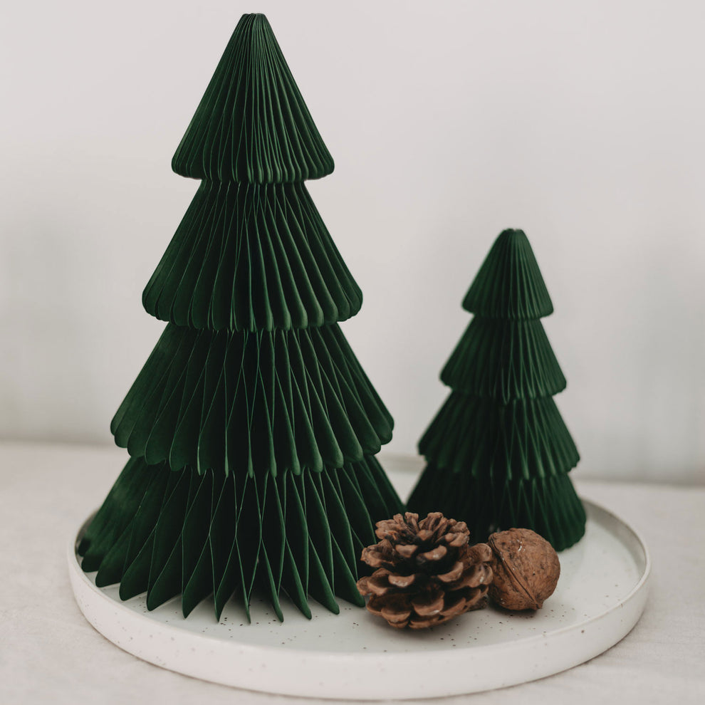 Minimalistisches Weihnachtsarrangement mit zwei dunkelgrünen Papiertannen in verschiedenen Größen auf einem weißen Teller, dekoriert mit einem Tannenzapfen und einer Walnuss.