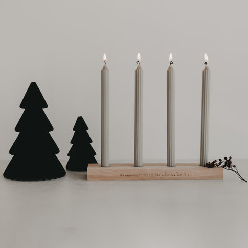 Schwarze Papiertannen mit Holz-Kerzenhalter und vier brennenden Kerzen – stilvolle, moderne Weihnachtsdeko auf Tischfläche.