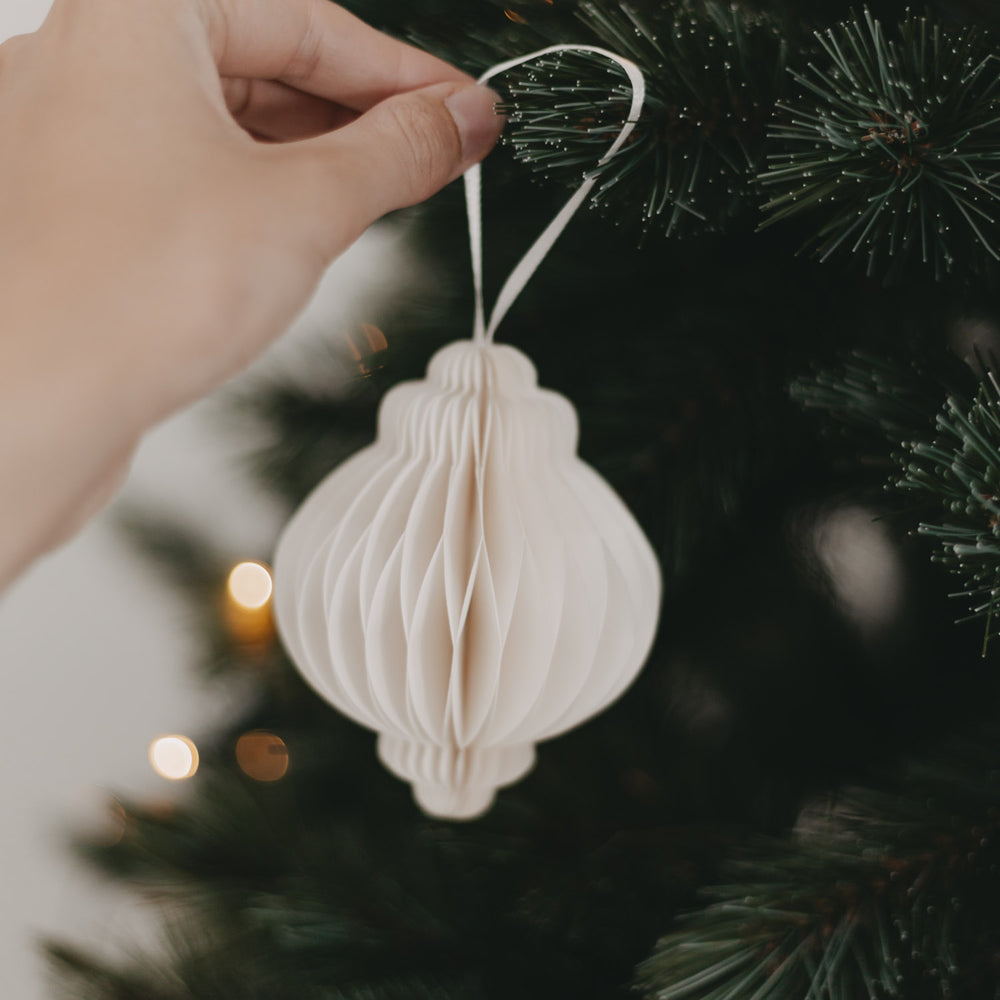 Hand hängt Papieranhänger in Naturfarbe mit weißem Band an den Weihnachtsbaum