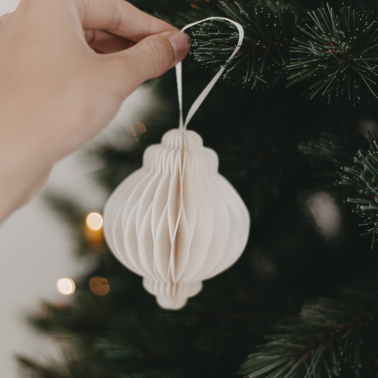 Hand hängt Papieranhänger in Naturfarbe mit weißem Band an den Weihnachtsbaum