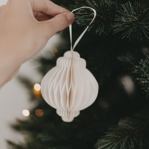 Hand hängt Papieranhänger in Naturfarbe mit weißem Band an den Weihnachtsbaum