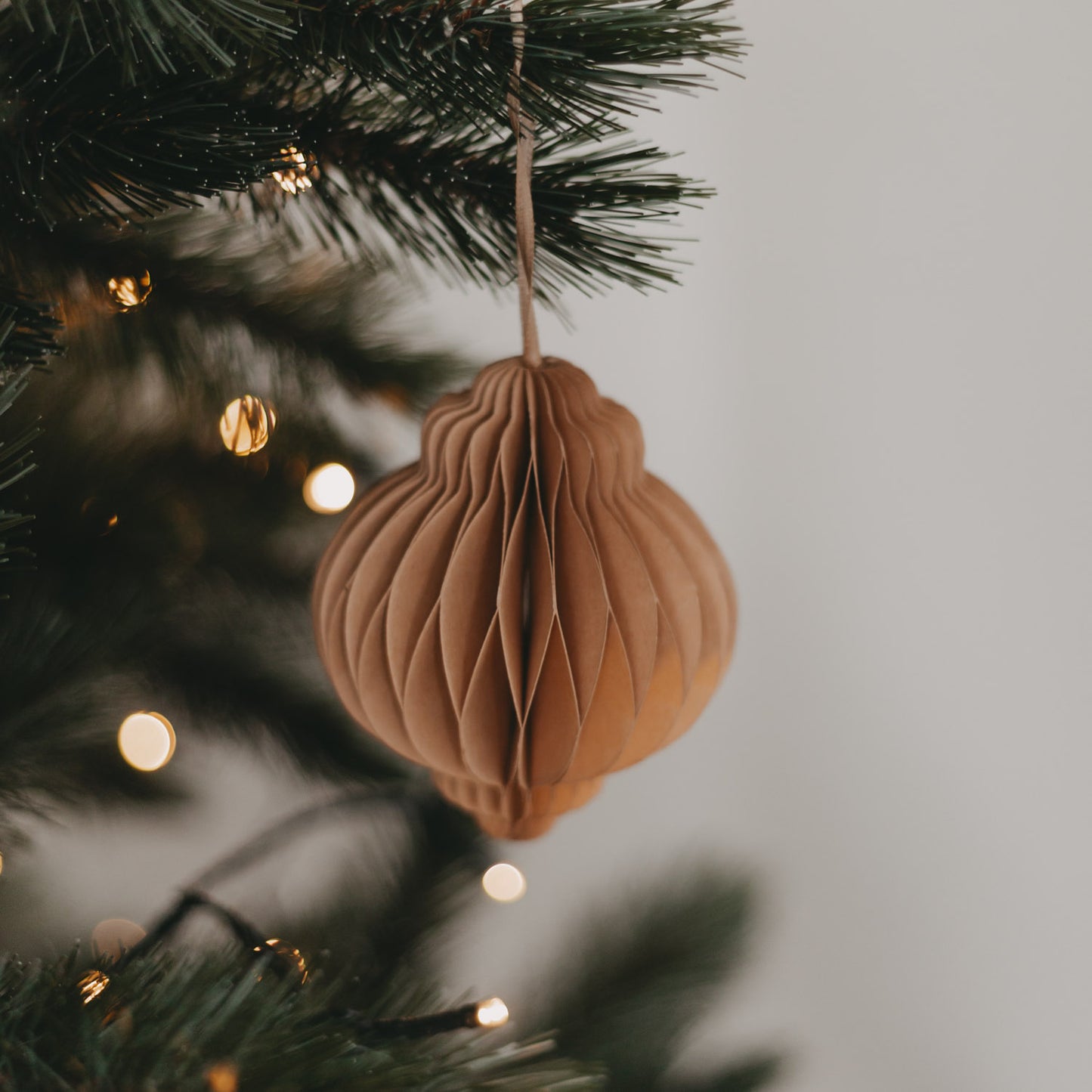 Brauner Papieranhänger dekorativ am Tannenbaum aufgehängt, mit sanfter Weihnachtsbeleuchtung im Hintergrund.