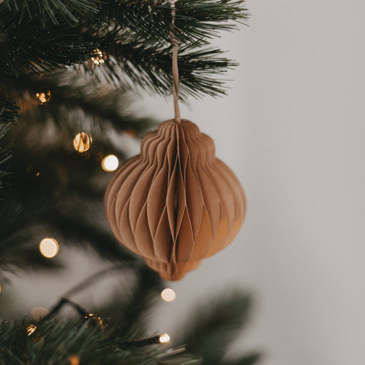 Brauner Papieranhänger dekorativ am Tannenbaum aufgehängt, mit sanfter Weihnachtsbeleuchtung im Hintergrund.