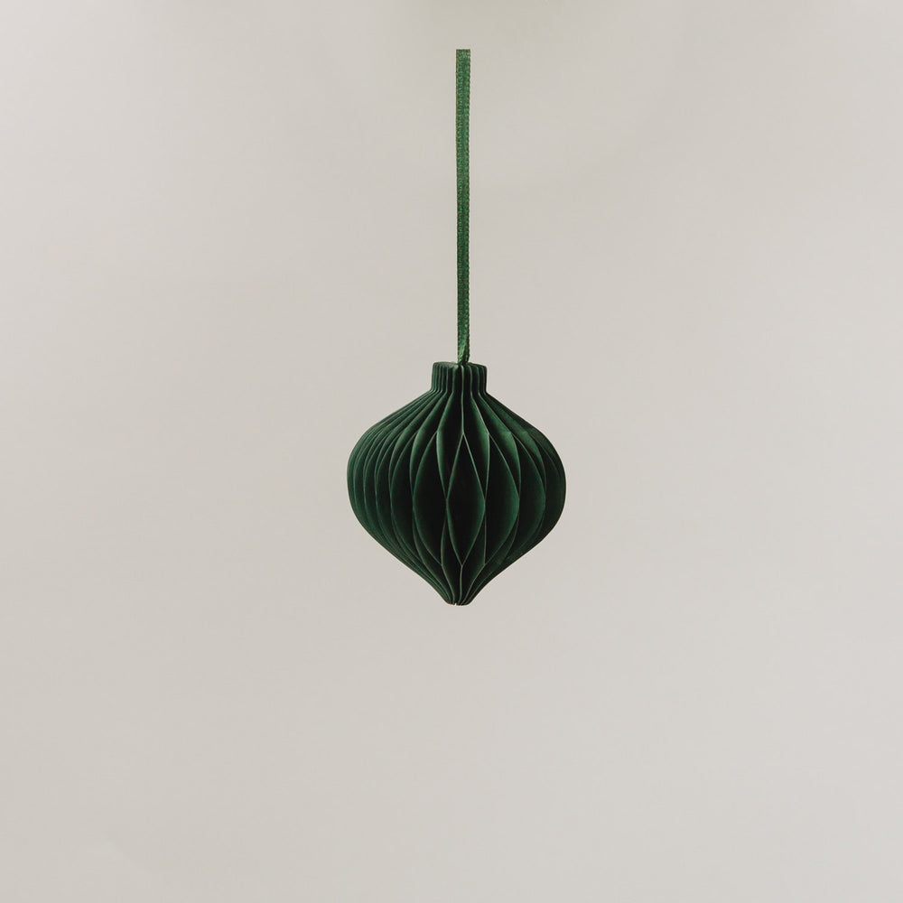Ein dunkelgrüner Papieranhänger in voller Wabenoptik hängt an einem Band vor hellem Hintergrund.