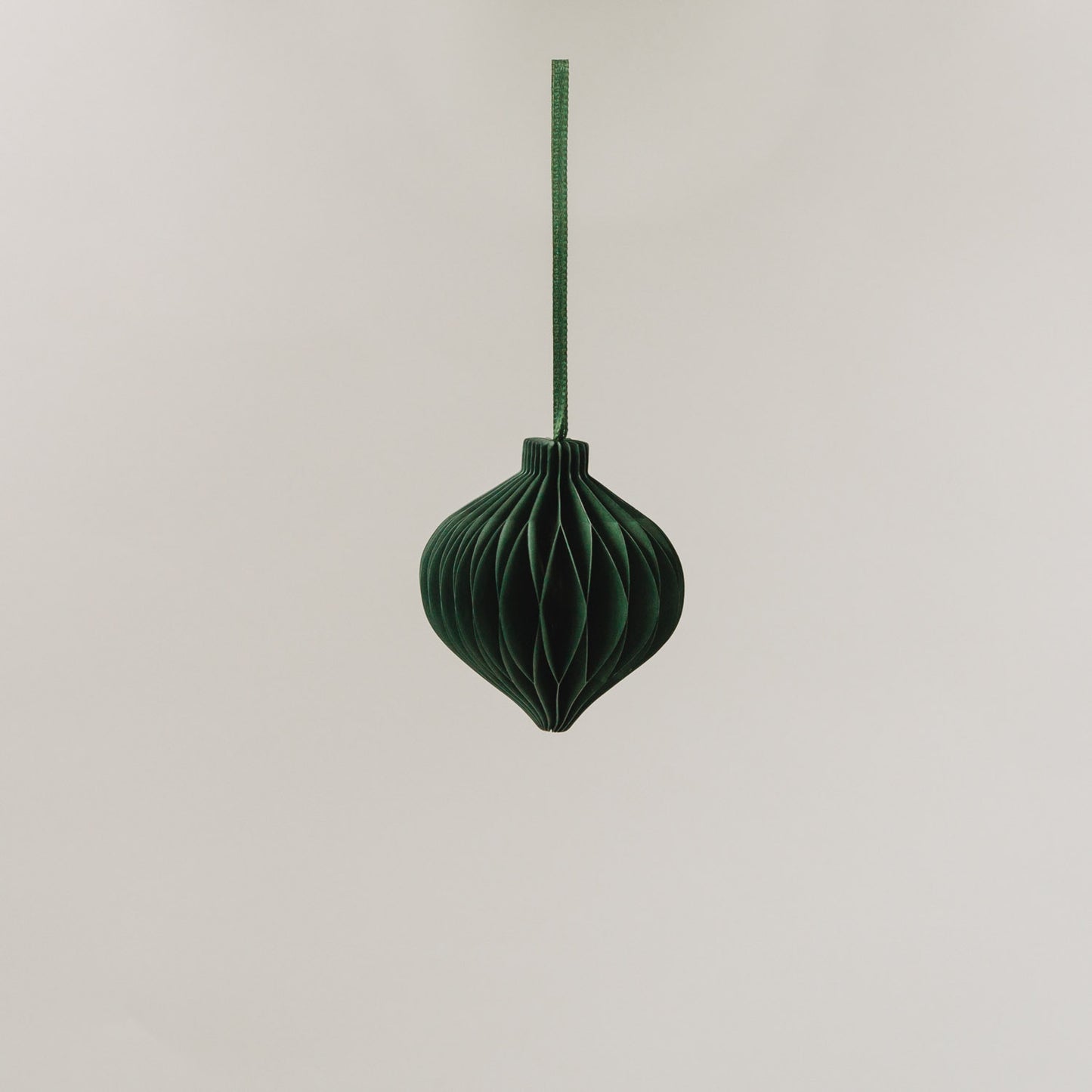 Ein dunkelgrüner Papieranhänger in voller Wabenoptik hängt an einem Band vor hellem Hintergrund.
