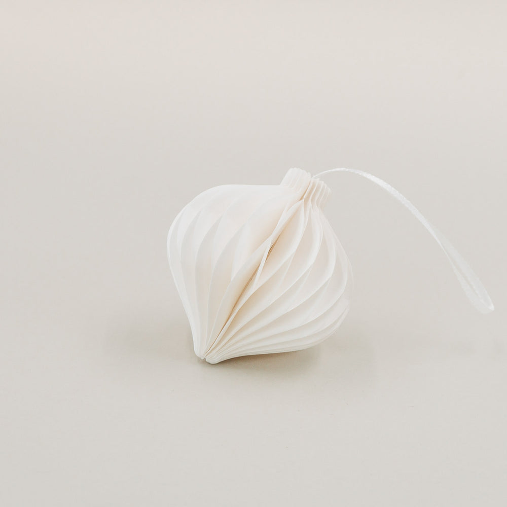 Ein weißer Papieranhänger in Tropfenform mit feiner Wabenoptik, liegend mit Band auf hellem Hintergrund