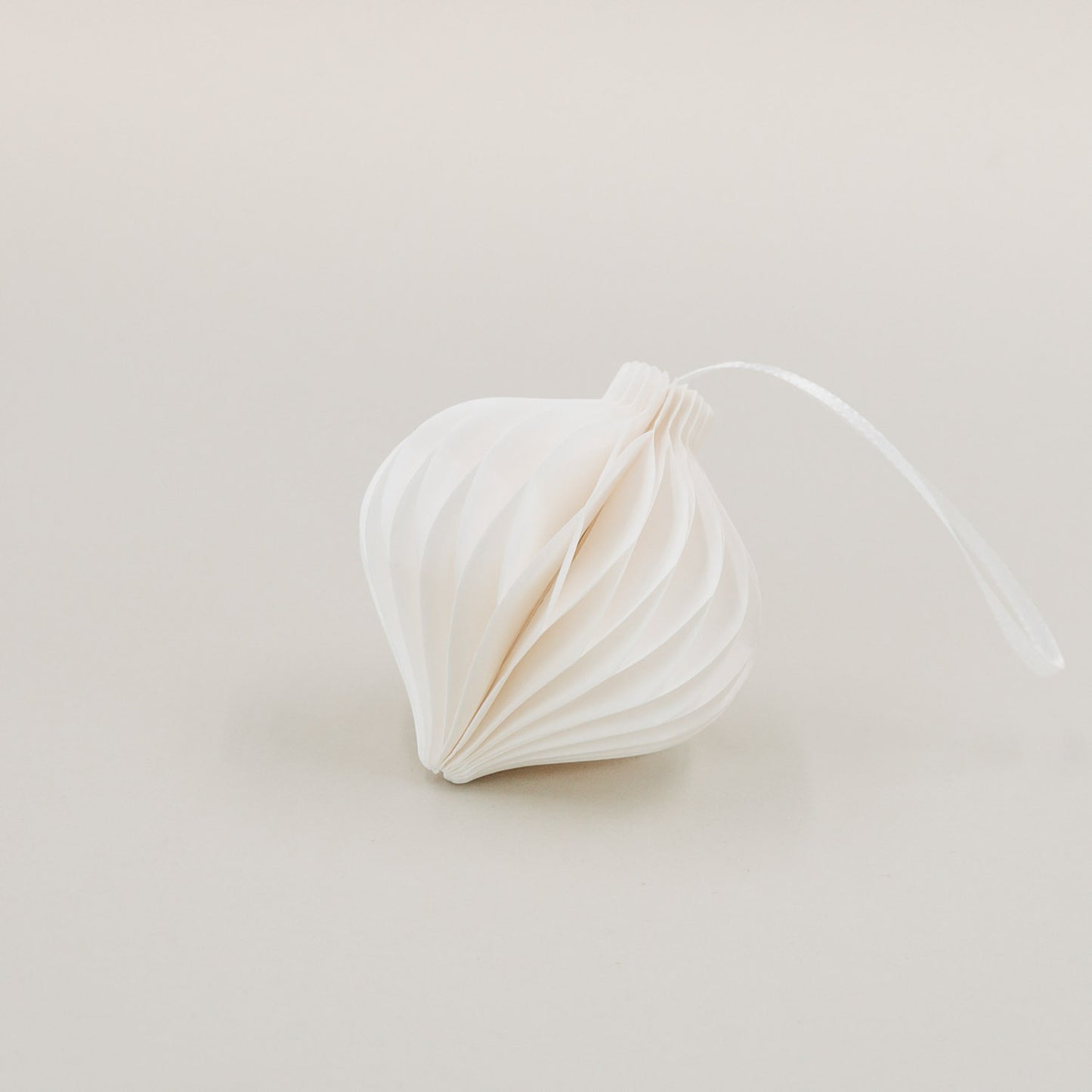 Ein weißer Papieranhänger in Tropfenform mit feiner Wabenoptik, liegend mit Band auf hellem Hintergrund