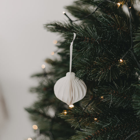 Weißer Anhänger hängt am Weihnachtsbaum zwischen grünen Zweigen und Lichterkette
