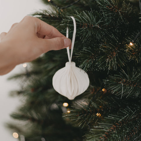 Hand hängt weißen Papieranhänger an einen Christbaumzweig – nachhaltige Dekoration im Einsatz