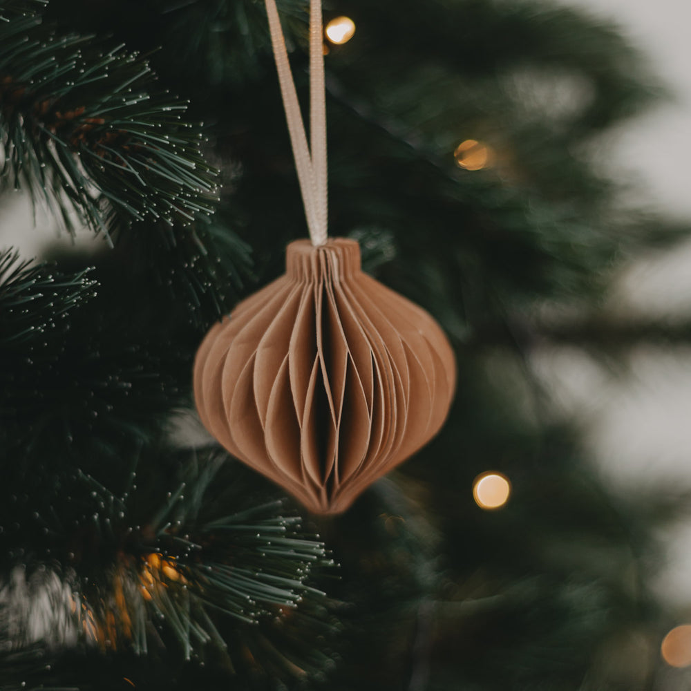 Brauner Papieranhänger dekorativ an einem Tannenzweig mit Lichterkette.