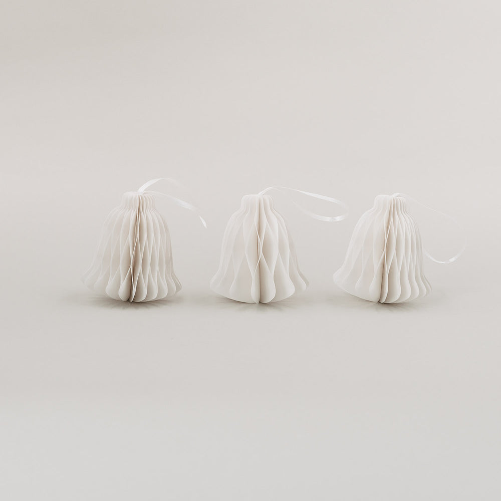 Drei weiße Papieranhänger in Glockenform mit Wabenoptik und Satinband auf hellem Hintergrund nebeneinander stehend.