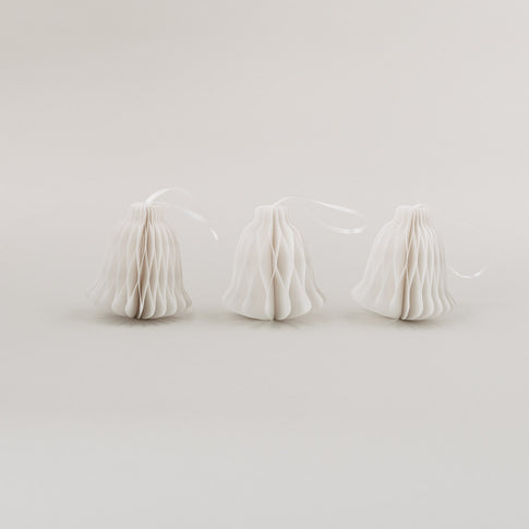 Drei weiße Papieranhänger in Glockenform mit Wabenoptik und Satinband auf hellem Hintergrund nebeneinander stehend.